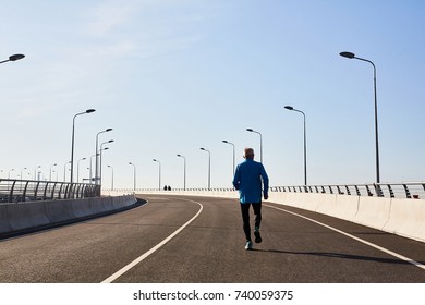 Back view of unrecognizable senior runner having intensive workout outdoors, cloudless blue sky on background