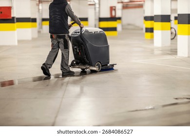 Back view of an unrecognizable washerman using scrubber machine for cleaning and maintenance garage floor.