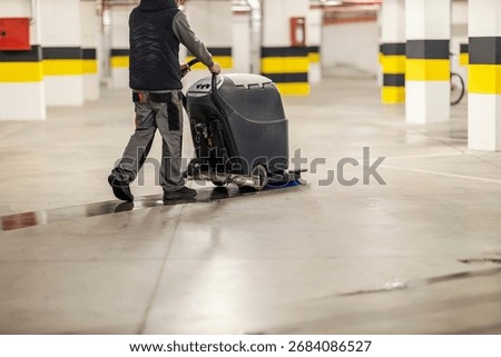 Back view of an unrecognizable washerman using scrubber machine for cleaning and maintenance garage floor.