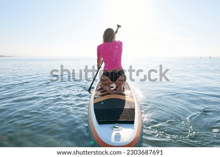 Back view of unrecognizable woman on paddle surf.Backlit