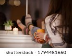 Back view of unrecognizable woman in warm clothes enjoying hot beverage and relaxing in cozy room in evening at home