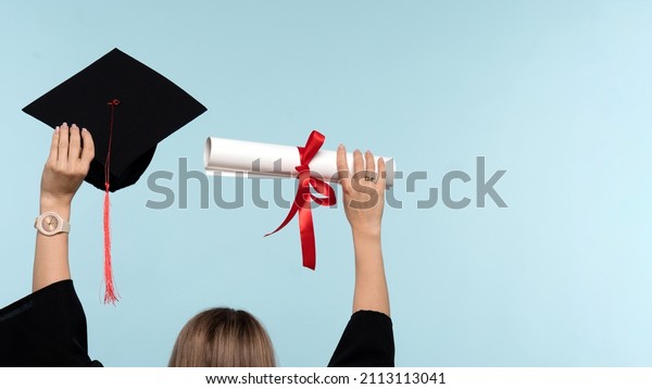 Back View Unrecognizable Woman Wearing Ceremony\
Robe Holding Certificate and Throwing Graduation Cap on Blue\
Background. Girl Celebrating Graduation and Getting Diploma.\
Graduate Cap and Degree\
Paper