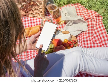 Back View Of Unrecognizable Woman In White Pants Outside Having Picnic And Using Smartphone Taking Photo. Summer Fun And Leisure. View From Behind