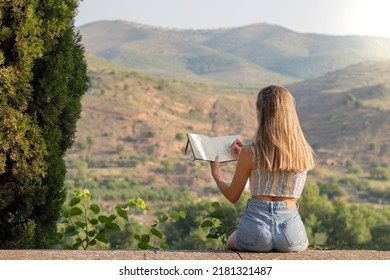 Back view unrecognizable young blonde woman drawing notebook the beautiful landscape she's admiring