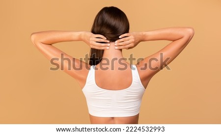 Back view of unrecognizable young lady self massaging her neck, rubbing skin while standing isolated over beige studio background, panorama, banner