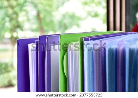 Back view of various plastic file folders for storing important documents in a file box for neatness and easy finding places near transparent glass window, blurred edited background.