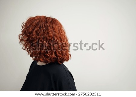 Back view of voluminous red curly hair with wide copy space on a plain light background for design.