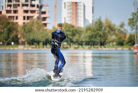 Back view of wakeboarder surfing on lake. Young surfer having fun wakeboarding in the cable park. Water sport, outdoor activity concept.