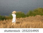 Back view of a white caucasian woman wearing a straw hat, standing against a clear blue sky, minimalist summer scene.