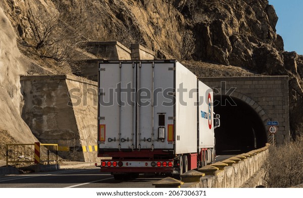 Back view of white truck belonging to the company\
Transtolk on the mountain road, at the entrance to the tunnel. Semi\
truck carrying goods on the tunnel road. Orsova, Romania, October\
30, 2021