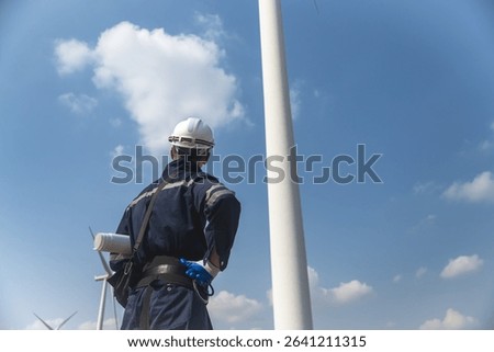 Back view wind turbine engineer man holding blueprint looking at turbine tower in windmill field