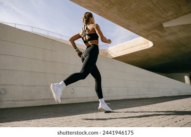 Back view of woman athlete in sportswear is running on buildings background. Active life concept - Powered by Shutterstock