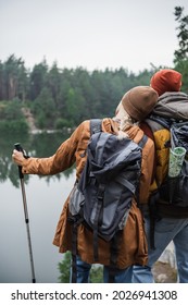 Back View Of Woman With Backpack Holding Hiking Stick And Leaning On Man Near At Lake