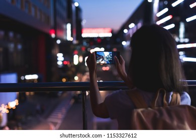 back view of woman with backpack taking picture of city on smartphone in hands at night - Powered by Shutterstock