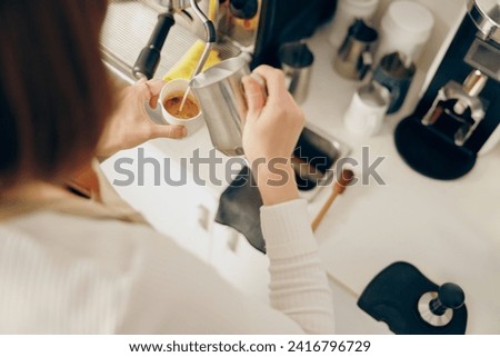 Back view of woman barista in apron pouring hot milk foam into coffee working in coffee shop