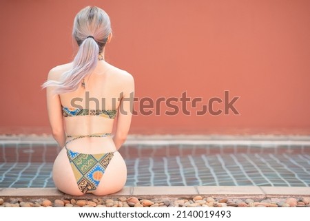 Back view of woman in bikini resting on the edge of the pool.