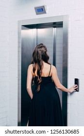 Back View Of Woman In Black Dress Pressing Elevator Button