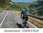 Back view of woman cyclist riding a road bike with a view of the mountains. Sport motivation.Female cyclist wearing a cycling kit and helmet. Carpathian Mountains, Transfăgărășan road in Romania.