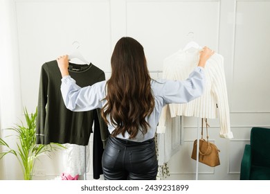 Back view of a woman deciding between two shirts hanging on a rack in a well-lit room - Powered by Shutterstock