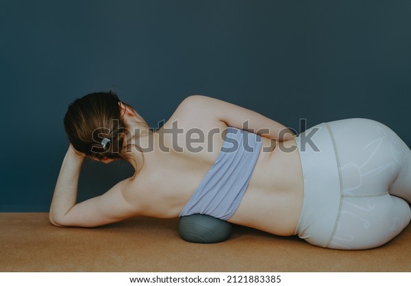 Back view of woman doing\
myofascial release on side ribs with cork roller for tension\
release. Self care routine, techniques at home, muscle release,\
pre-sport MFR