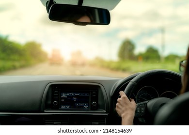 Back view of a woman driving car for summer road trip travel. Car driving with safety on asphalt road. Driver hand holding steering wheel for control car. Inside view of car. Dashboard and windshield.