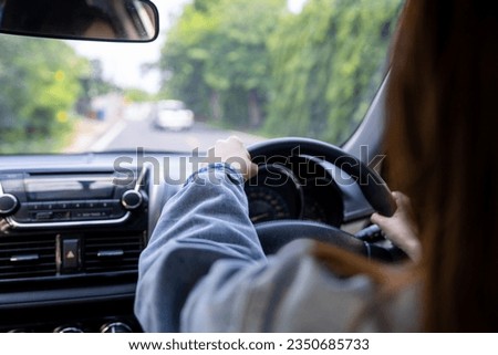 Back view of a woman driving car for summer road trip travel. Driver hand holding steering wheel for control car. Safe driving concept.