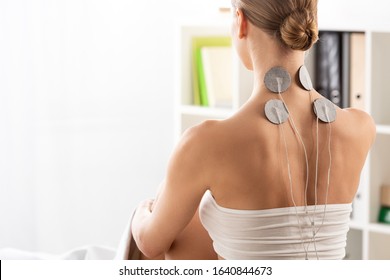 Back view of woman with electrodes on neck during electrode treatment in clinic