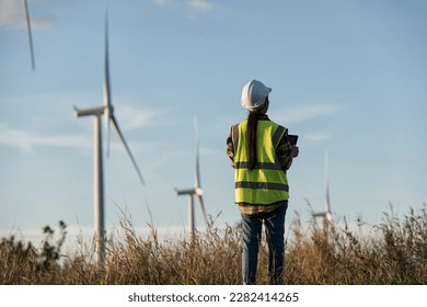 Back view of woman engineer standing against turbines on wind turbine farm. - Powered by Shutterstock