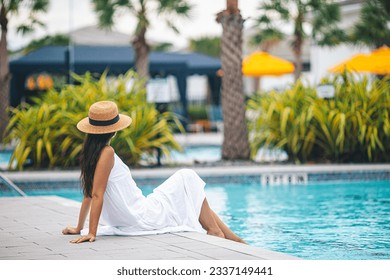 Back view of woman in hat relaxing by the outdoor swimming pool in a luxurious hotel resort enjoying summer vacation - Powered by Shutterstock