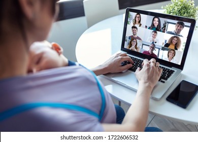 Back view of woman and her baby son doing online meeting with coworkers on video call on laptop at home. - Shutterstock ID 1722606532