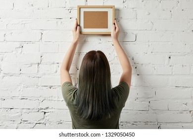 Back View Of Woman Holding Blank Brown Frame In Hands