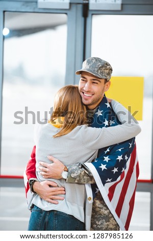 back view of woman hugging boyfriend in military uniform with american flag in airport 