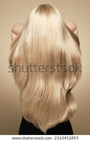 Back view of woman with long beautiful blond hair isolated on beige background. Dyeing and hair care. Shiny smooth blonde hair