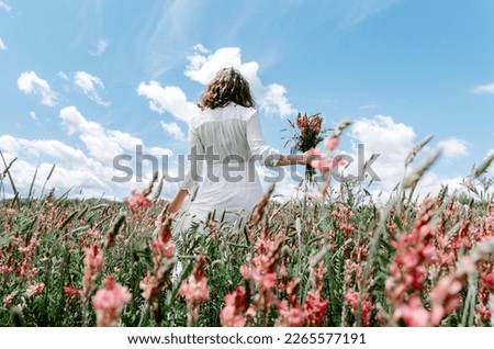 Back view of woman in long white dress with a wildflower bouquet in pink flower field
