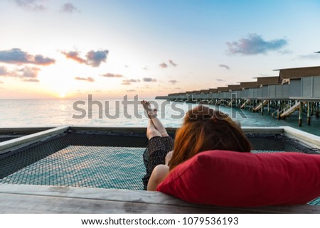 Back of view woman lying on terrace looking on sunset with villas over water in Maldives feeling relax and comfortable in Vacation summer holiday