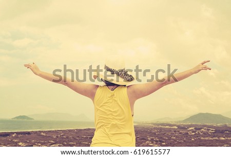 Back view of a woman with open arms on vacation wearing beach hat with a coastal landscape on the background. Feeling of freedom. Photo taken in Florianopolis on Dunas da Joaquina, Brazil.