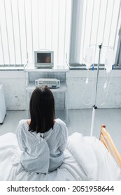 Back View Of Woman In Patient Gown Sitting On Hospital Bed