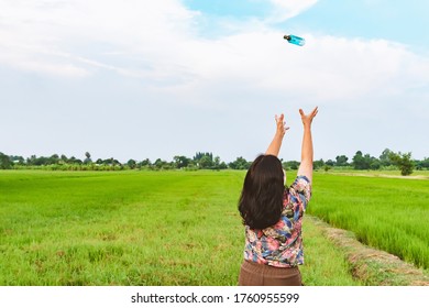 Back view of woman raises her arms to wait for alcohol gel bottle falling from the sky in the rice field.Campaign to prevent the spread of the Corona virus(Covid-19).New normal concept.Selective focus - Shutterstock ID 1760955599