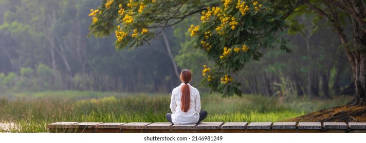 Back View Of Woman Relaxingly Practicing Meditation In The Public Park To Attain Happiness From Inner Peace Wisdom With Yellow Flower Blossom In Summer