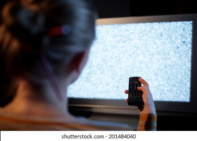 Back View Of Woman With Remote Control In Front Of TV Set With Noise On The Screen