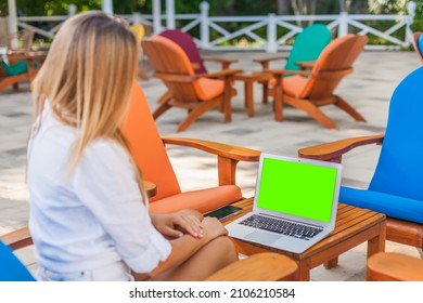 Back View Of A Woman Sitting In The Outdoor Cafe Using A Laptop With A Green Screen. She's Watching Something Or Talking To Her Friends Or Family Using Videochat.