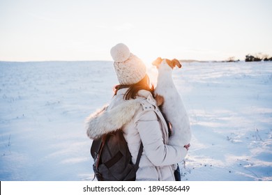 back view of woman in snowy mountain wearing modern coat at sunset. Holding cute jack russell dog in arms. winter season. nature at sunset - Powered by Shutterstock