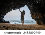 The back view of a woman standing in a cave by the sea.