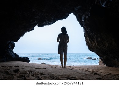 The back view of a woman standing in a cave by the sea. - Powered by Shutterstock
