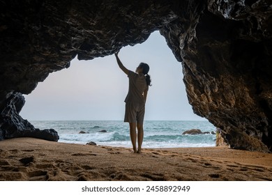 The back view of a woman standing in a cave by the sea. - Powered by Shutterstock