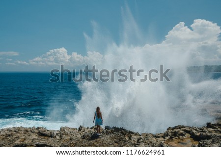 Back view woman standing in front of the sea during a storm with a huge wave. Back view young girl  on the rocks near the wild ocean