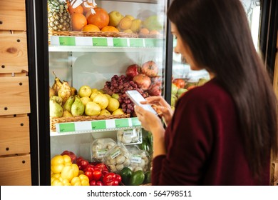 Back View Of Woman Standing And Using Cell Phone In Grocery Shop