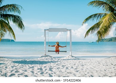 Back view of woman swinging on swing on white sandy beach in tropical destination. Enjoying amazing view on blue sea in sunny day in Cambodia. Girl relaxing on exotic vacation. Summer holiday concept.
