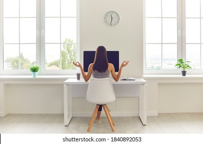 Back View Of Woman Taking Break From Office Work And Meditating Sitting In Modern Workspace At Table With Desktop Computer And Cup Of Coffee To Go. Concepts Of Corporate Wellbeing And Stress Relief