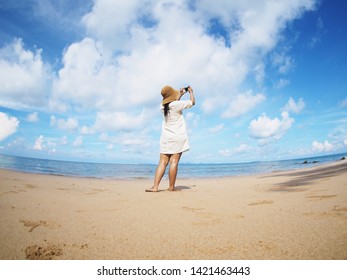 Back View Woman Taking Photograph On The Beach. Happy People On Summer Holiday Vacation Concept. Fish Eye Lens Distortion